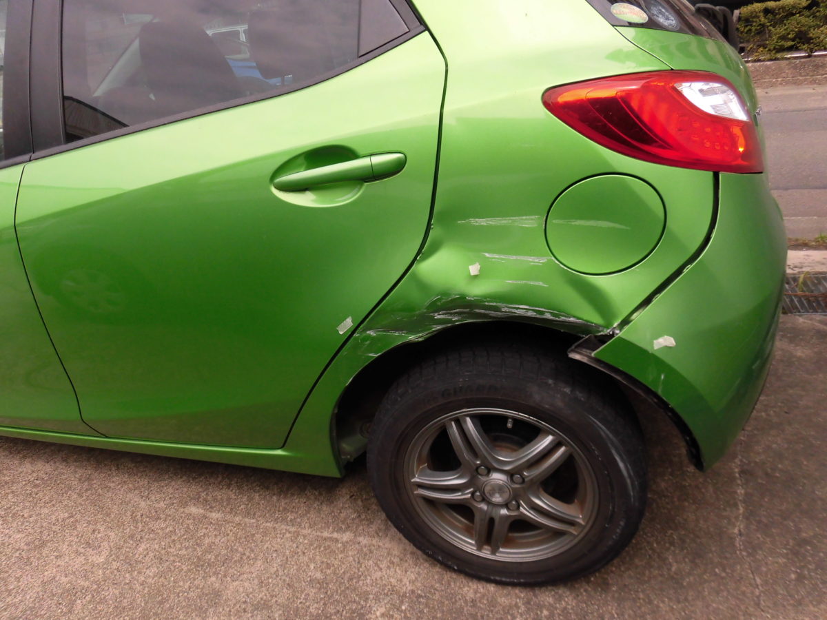 キレイなグリーンのマツダデミオの左後ろドアとクオーター、バンパーが事故でキズやヘコミがひどい状態の写真です。